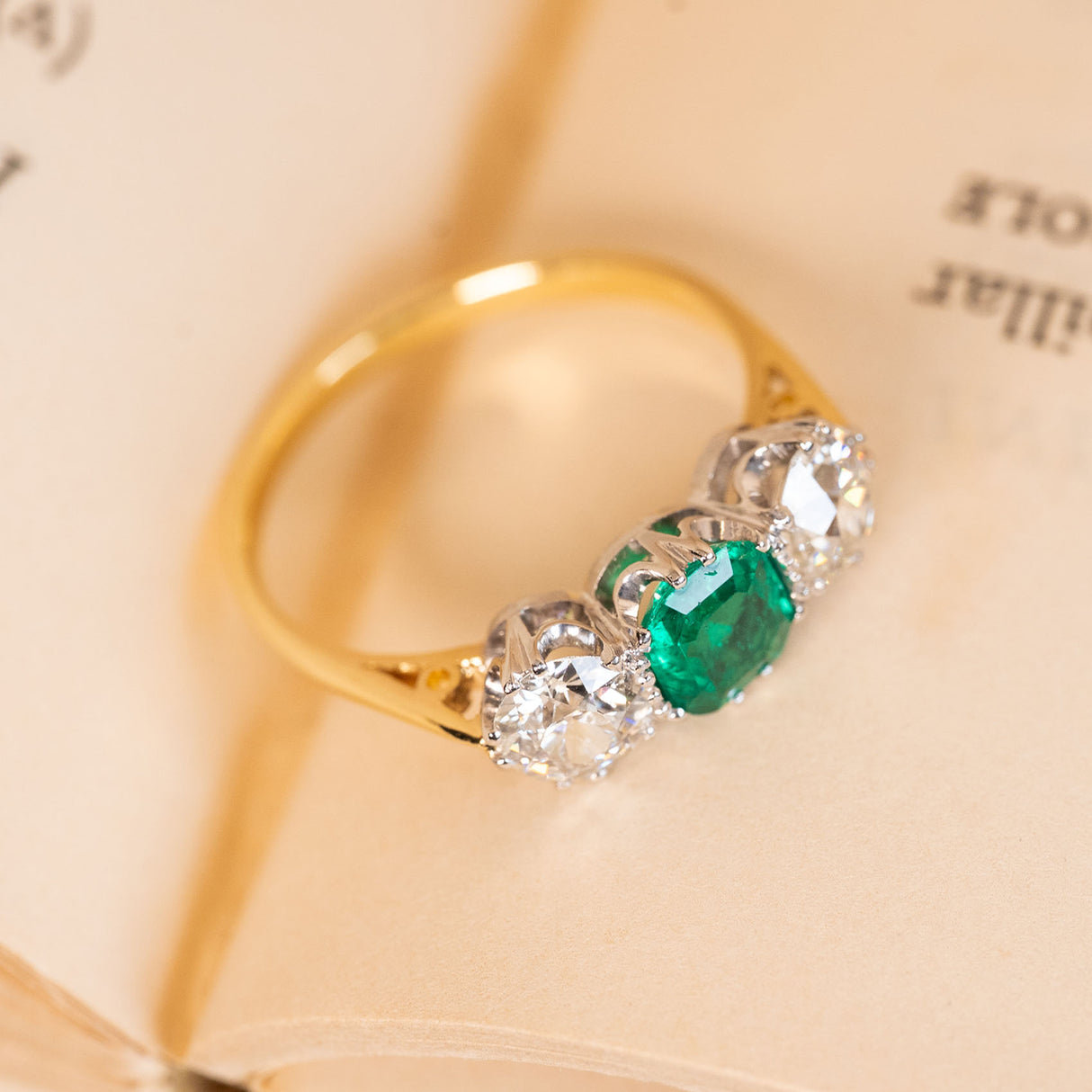 Antique three-stone ring with a rich green emerald centre stone and old-cut diamond accents, crafted in classic Edwardian style.