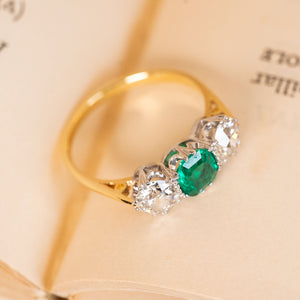 Antique three-stone ring with a rich green emerald centre stone and old-cut diamond accents, crafted in classic Edwardian style.