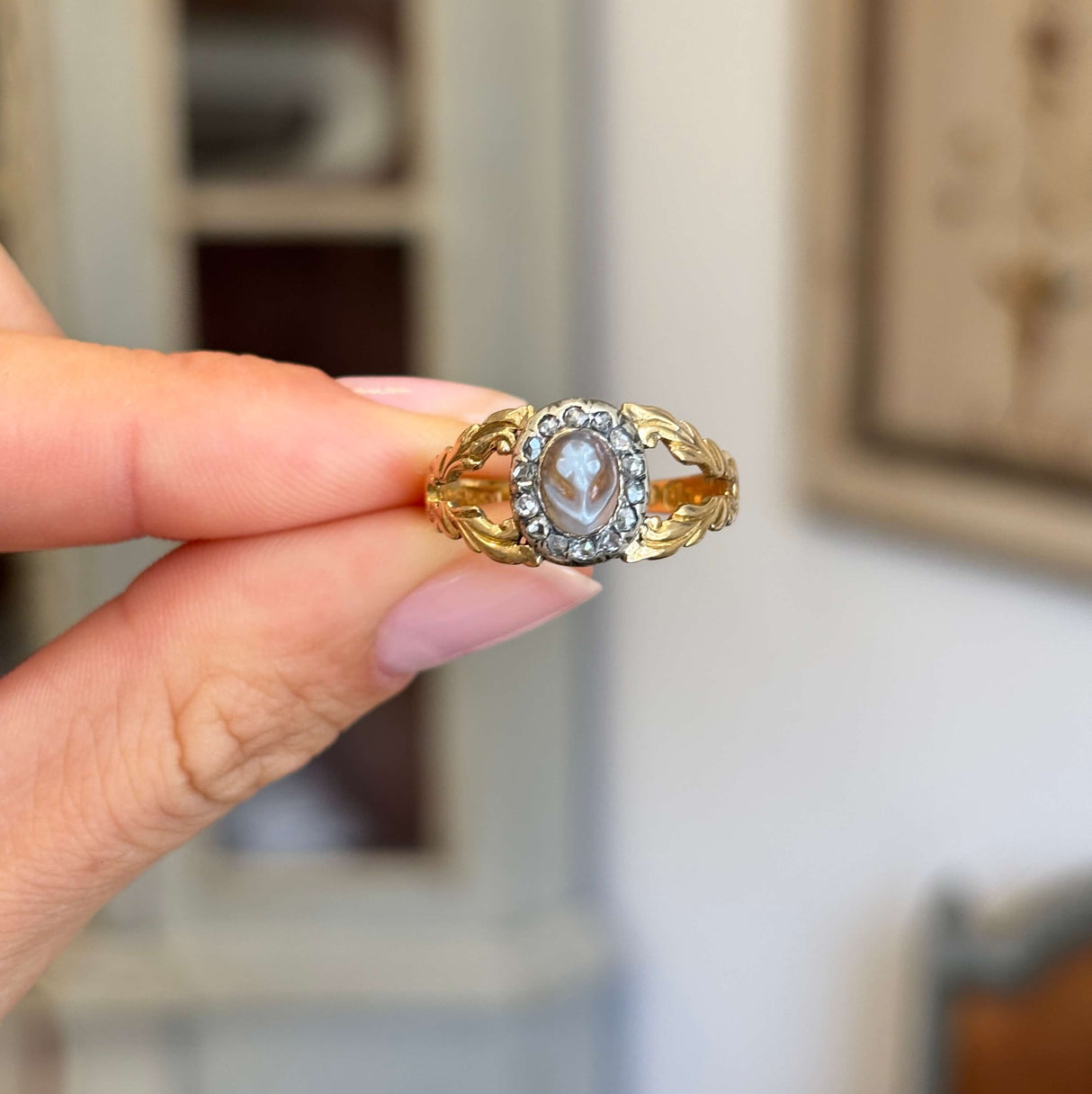 Antique Georgian forget-me-not cameo cluster ring featuring a hand-carved forget-me-not cameo surrounded by a decorative cluster setting, held by hand.