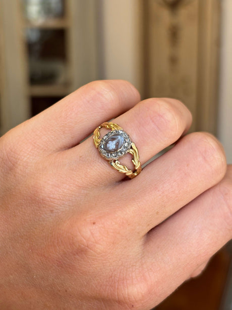Antique Georgian forget-me-not cameo cluster ring with a carved forget-me-not cameo and decorative cluster setting, worn on a hand.