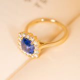 Antique-inspired sapphire and diamond cluster engagement ring featuring a violet-blue cushion cut sapphire encircled by diamonds.