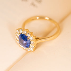Antique-inspired sapphire and diamond cluster engagement ring featuring a violet-blue cushion cut sapphire encircled by diamonds.