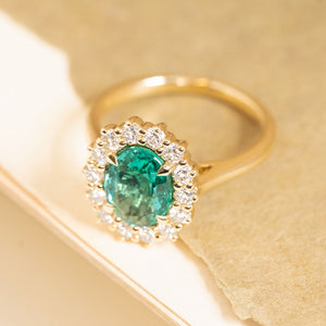 Antique-inspired emerald and diamond cluster engagement ring set with an oval-cut emerald framed by brilliant-cut diamonds.