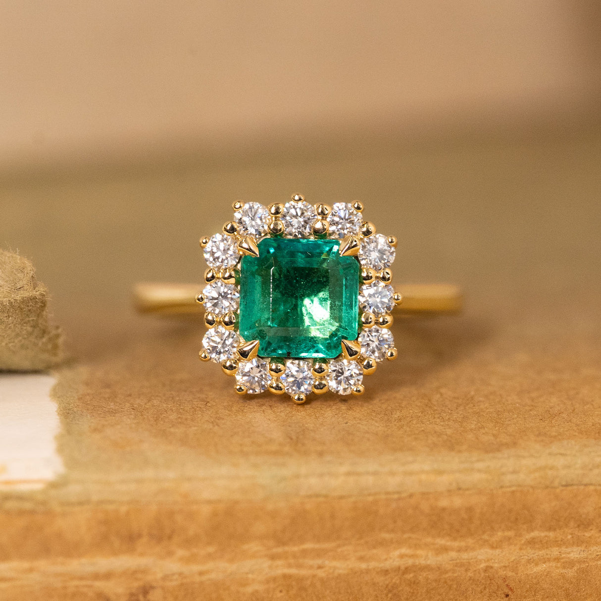 Antique-inspired emerald and diamond cluster engagement ring featuring an emerald-cut emerald surrounded by brilliant-cut diamonds in yellow gold.