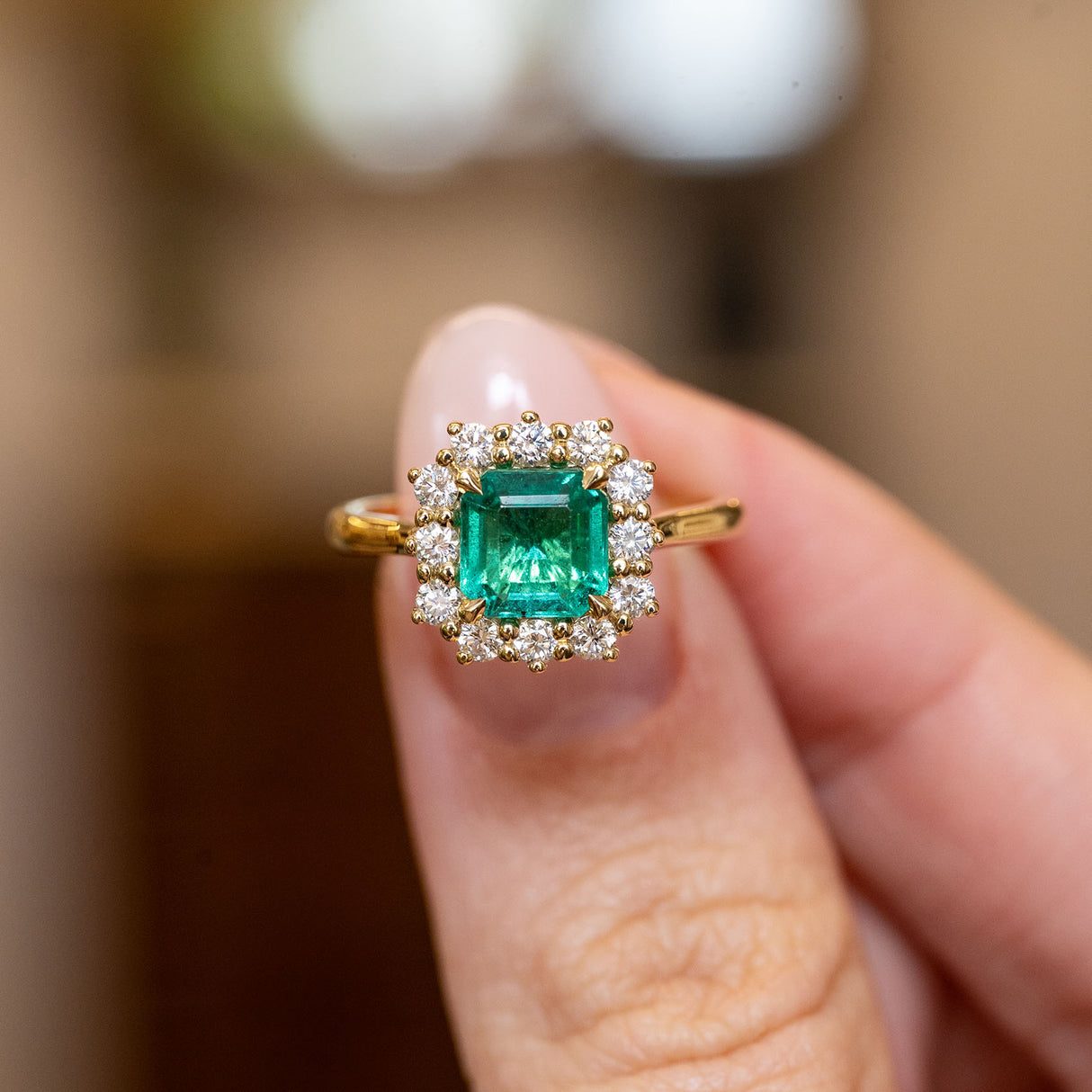 Antique-inspired emerald and diamond cluster engagement ring featuring an emerald-cut emerald surrounded by brilliant-cut diamonds in yellow gold.