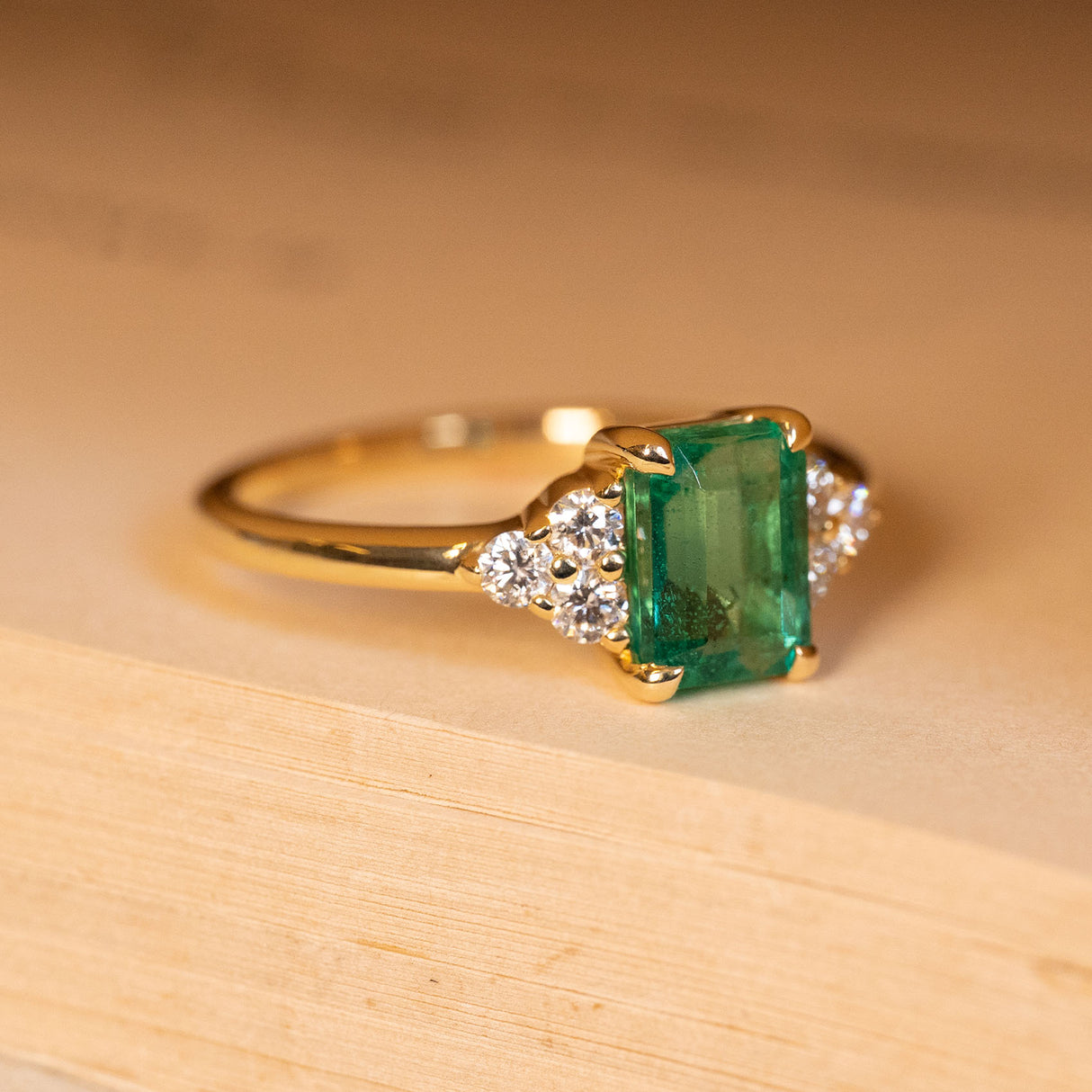 Antique inspired emerald and diamond cluster trefoil engagement ring highlighting the emerald-cut emerald and trefoil diamond shoulder clusters.
