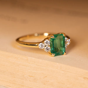 Antique inspired emerald and diamond cluster trefoil engagement ring highlighting the emerald-cut emerald and trefoil diamond shoulder clusters.