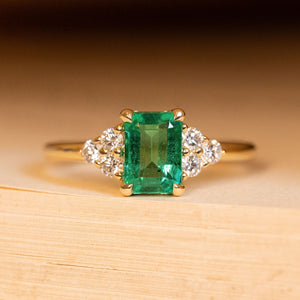 Antique inspired emerald and diamond cluster trefoil engagement ring featuring an emerald-cut emerald with trefoil diamond clusters on each shoulder in yellow gold.