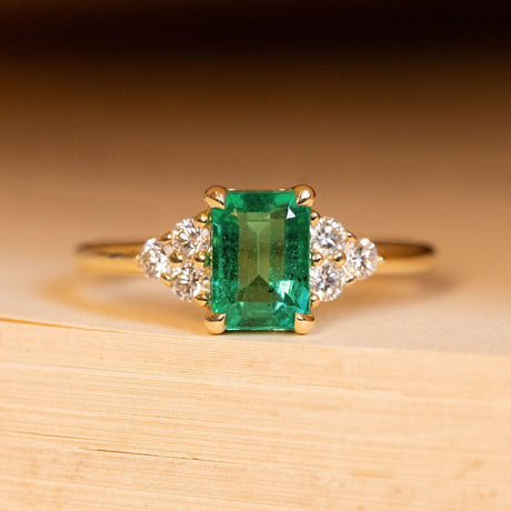 Antique inspired emerald and diamond cluster trefoil engagement ring featuring an emerald-cut emerald with trefoil diamond clusters on each shoulder in yellow gold.