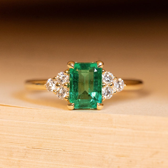 Antique inspired emerald and diamond cluster trefoil engagement ring featuring an emerald-cut emerald with trefoil diamond clusters on each shoulder in yellow gold.