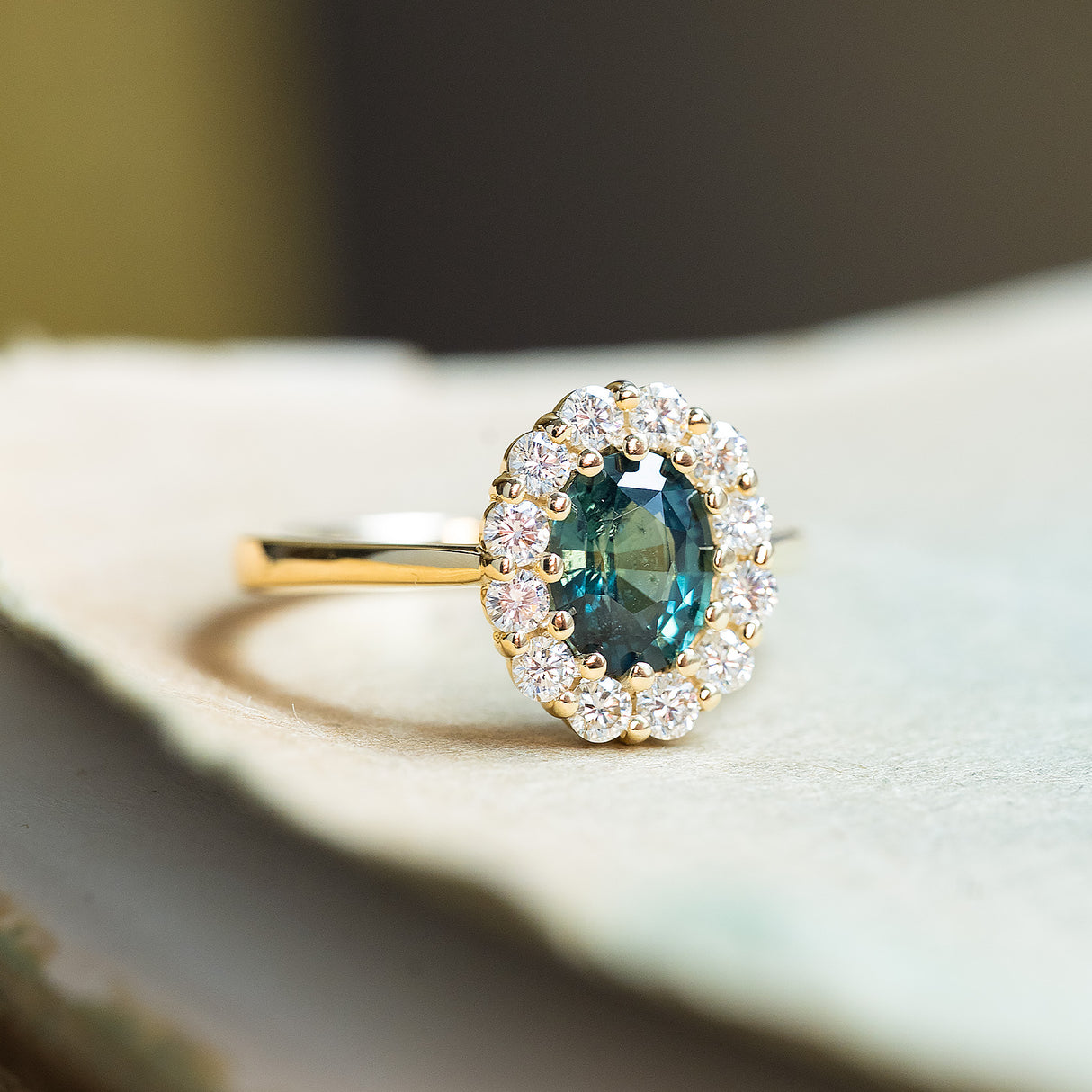 Green sapphire and diamond cluster engagement ring with oval-cut sapphire and gold band.