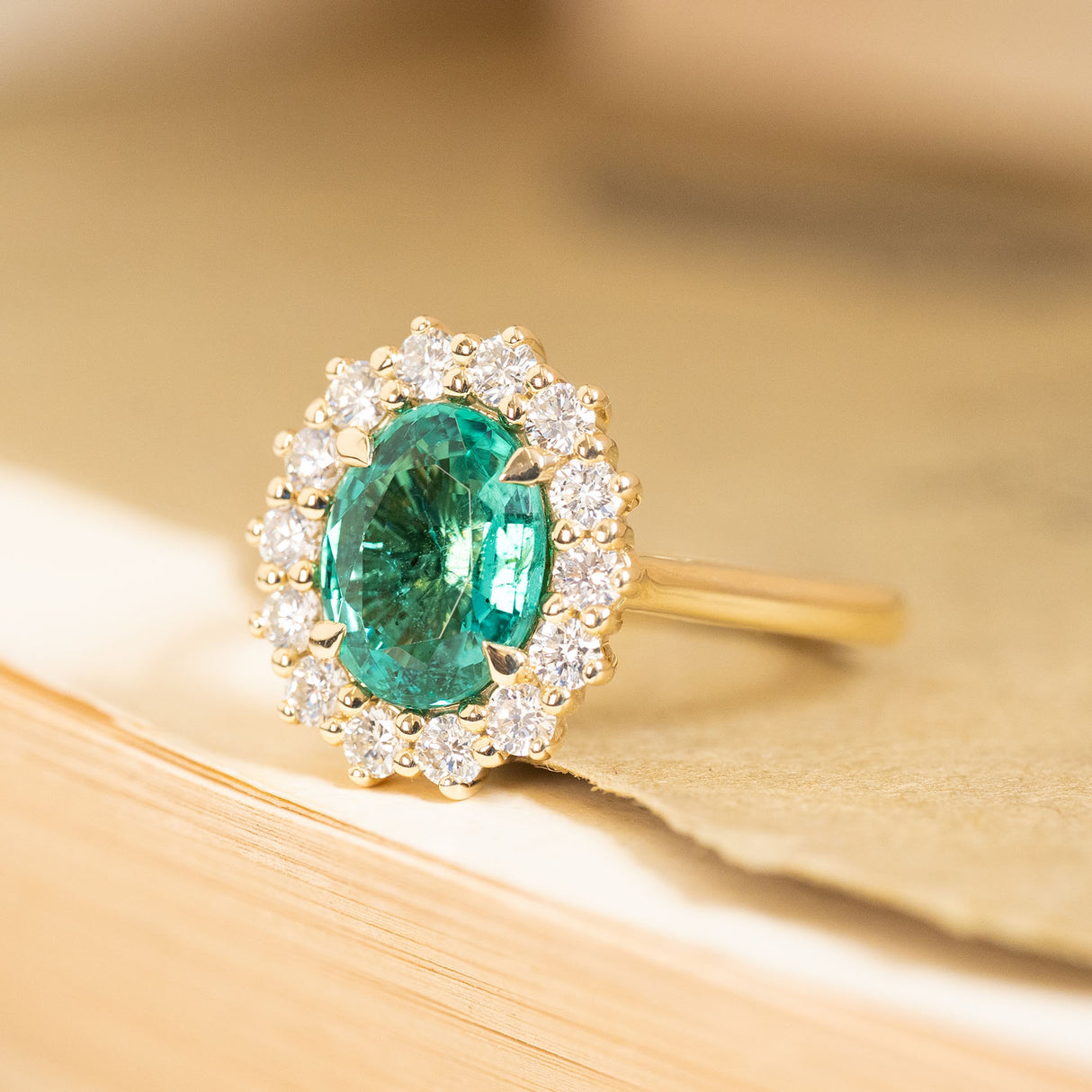 Antique-inspired oval-cut emerald engagement ring with a sparkling diamond cluster halo and elegant yellow gold band.