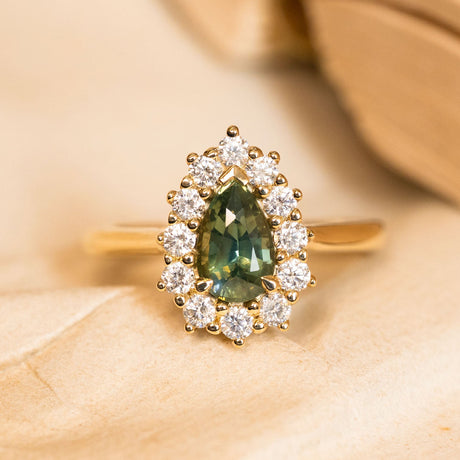 Antique-inspired pear-cut green sapphire and diamond cluster engagement ring featuring a green sapphire surrounded by a sparkling diamond halo in yellow gold.