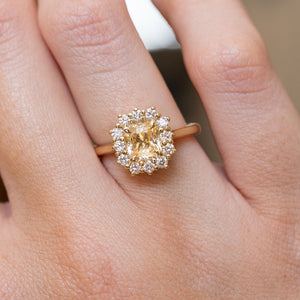 Antique inspired primrose-yellow sapphire and diamond cluster engagement ring shown on the finger, highlighting the oval yellow sapphire and diamond halo.