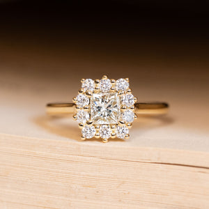 Antique inspired princess-cut diamond cluster engagement ring featuring a princess-cut diamond surrounded by a cluster of brilliant-cut diamonds in yellow gold.