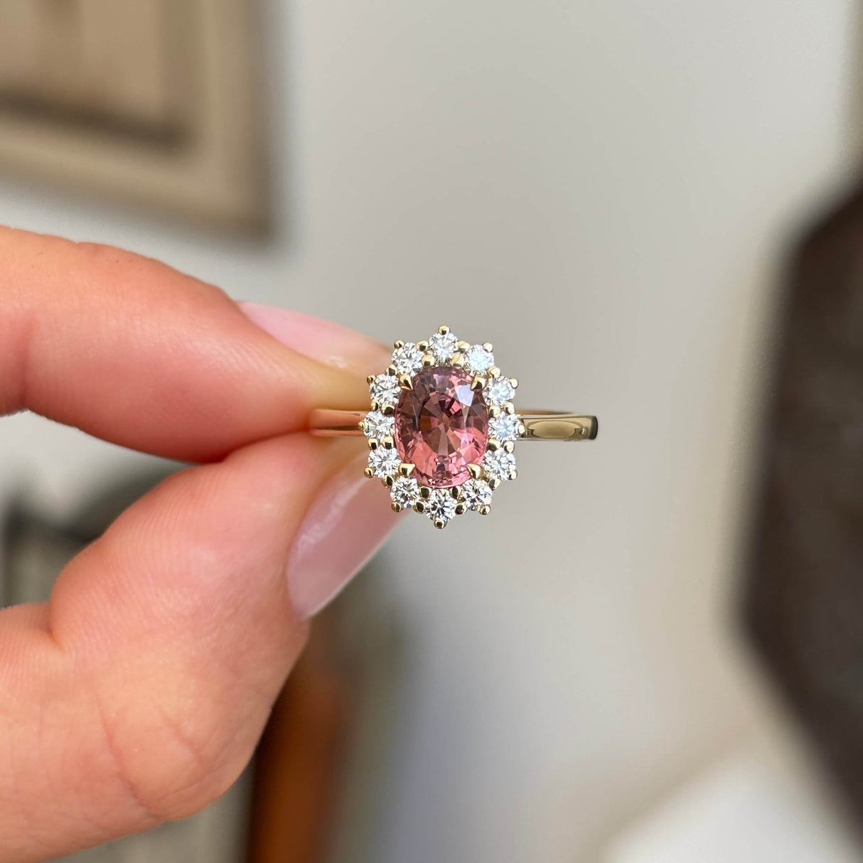 Antique-inspired rose-pink tourmaline and diamond cluster engagement ring featuring an oval rose-pink tourmaline surrounded by brilliant-cut diamonds, held by hand.