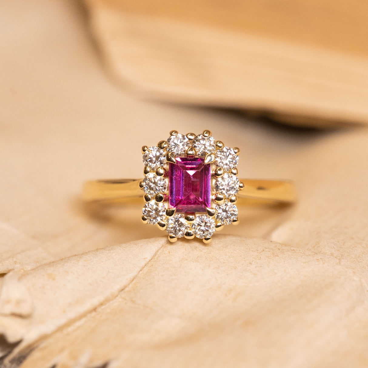 Antique-inspired rectangular step-cut ruby and diamond cluster engagement ring featuring a vivid red ruby surrounded by brilliant-cut diamonds in yellow gold.