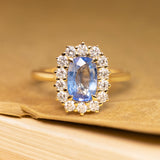 Antique-inspired engagement ring featuring an elongated sky blue sapphire surrounded by a sparkling diamond cluster in yellow gold.