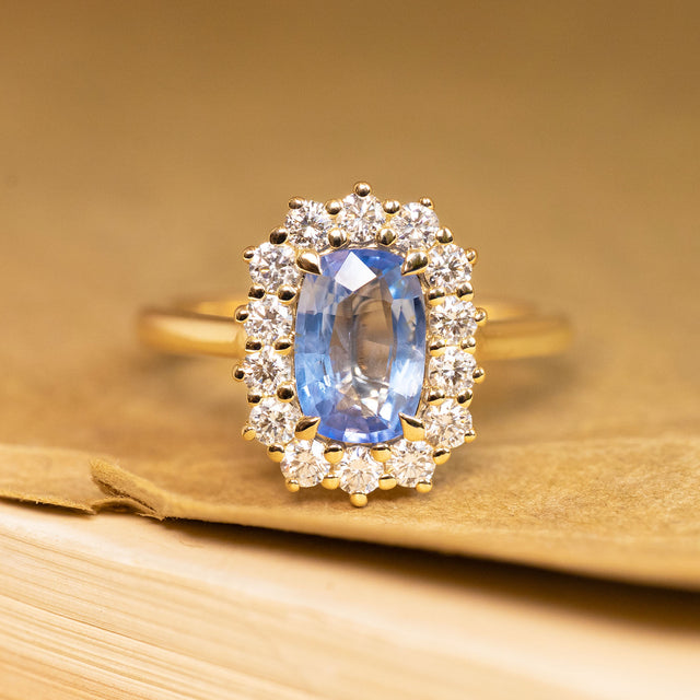 Antique-inspired engagement ring featuring an elongated sky blue sapphire surrounded by a sparkling diamond cluster in yellow gold.