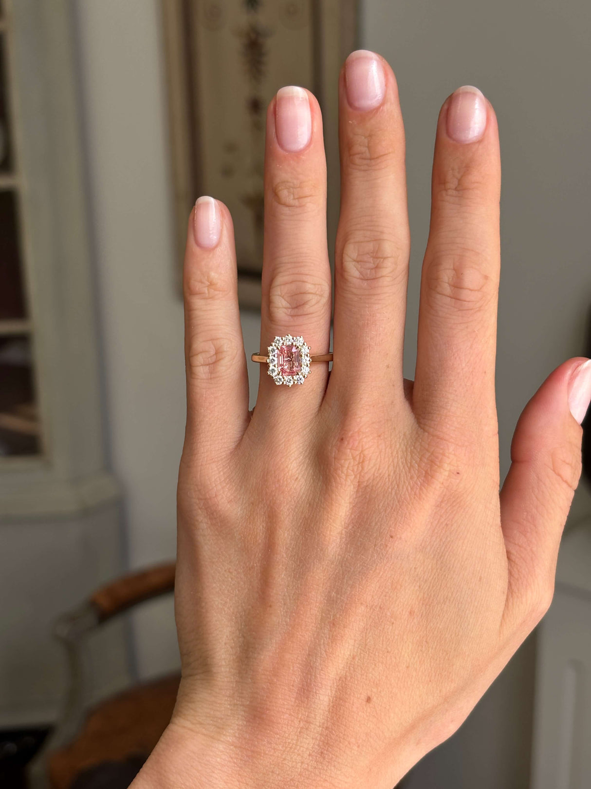 Antique-inspired sunset pink sapphire and diamond cluster engagement ring with an octagon-cut sunset pink sapphire centre stone and diamond halo, displayed on a hand.
