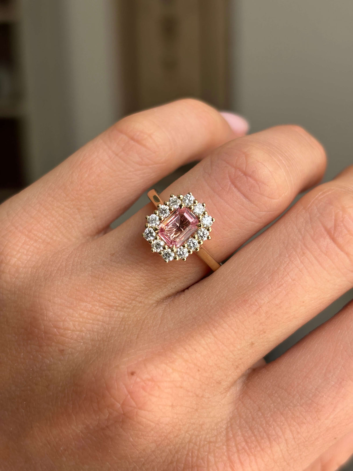 Antique-inspired sunset pink sapphire and diamond cluster engagement ring featuring an octagon-cut sunset pink sapphire encircled by brilliant-cut diamonds, worn on a hand.