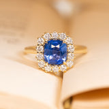 Antique-inspired violet-blue cushion cut sapphire and diamond cluster engagement ring in yellow gold.