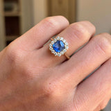 Close-up of an antique-inspired violet-blue cushion cut Sri Lankan sapphire and diamond cluster engagement ring in yellow gold, showcasing the vivid sapphire, sparkling diamond halo and refined craftsmanship.