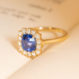 Cushion cut violet-blue sapphire engagement ring framed by a sparkling diamond cluster and set in yellow gold.