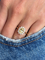 Antique-inspired yellow sapphire and diamond cluster engagement ring with an oval yellow sapphire centre stone and sparkling diamond halo, worn on a hand against a denim background