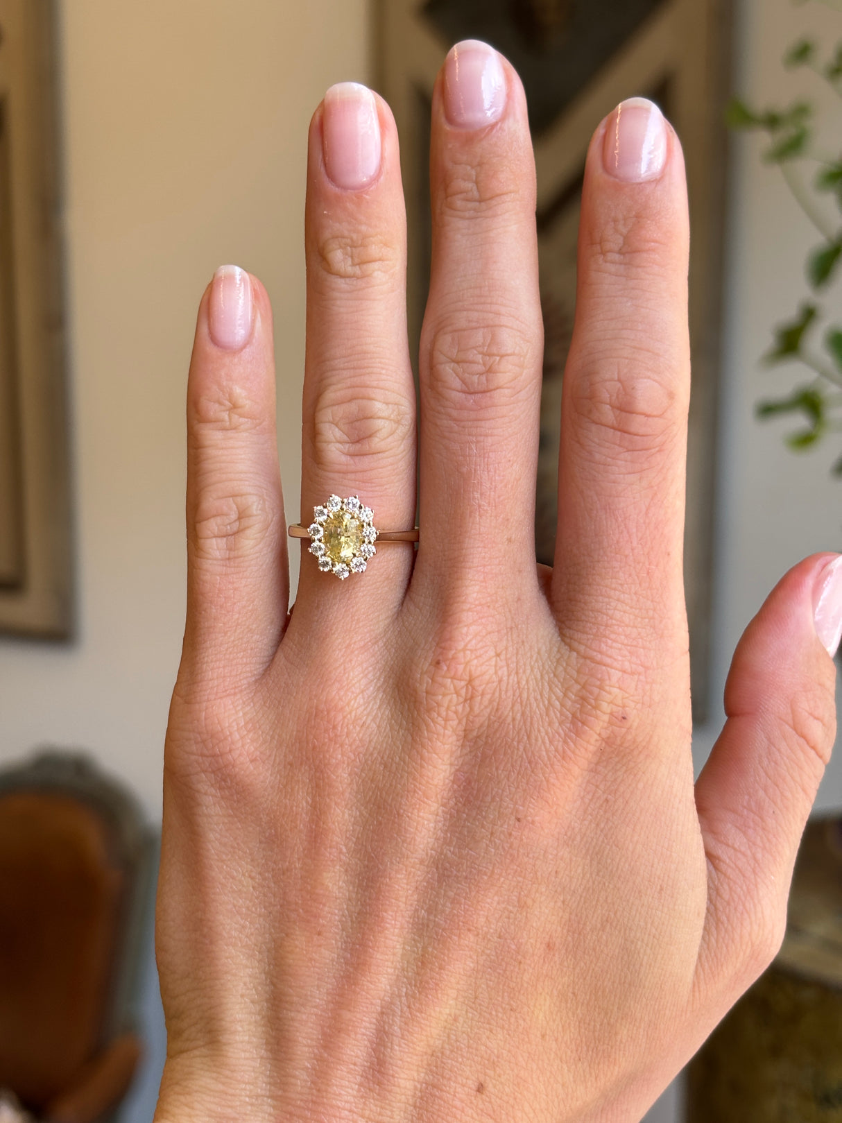 Antique-inspired yellow sapphire and diamond cluster engagement ring with an oval yellow sapphire centre stone and diamond halo, displayed on a hand.