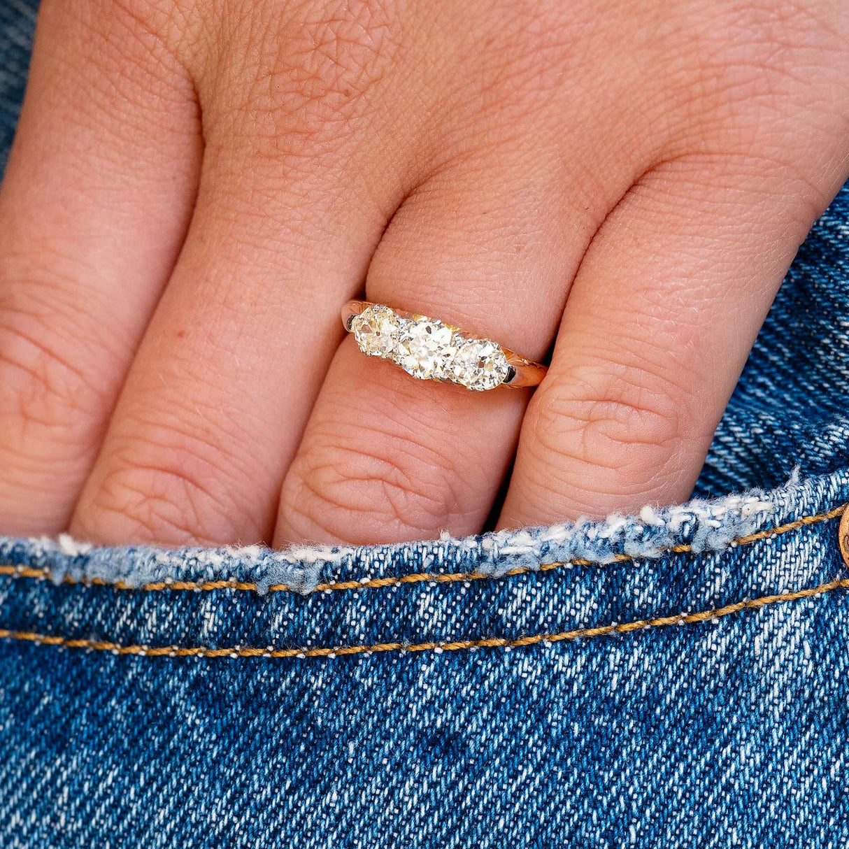 Close-up of a hand wearing a diamond ring with a blue denim jeans pocket.