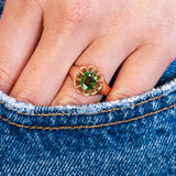 Close up of a hand wearing a ring with a green zircon with a denim pocket detail.