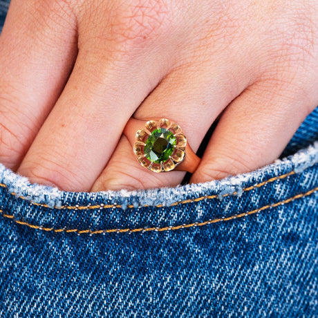 Close up of a hand wearing a ring with a green zircon with a denim pocket detail.
