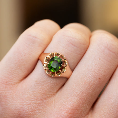 Gold ring with a green zircon on a hand against a blurred background.