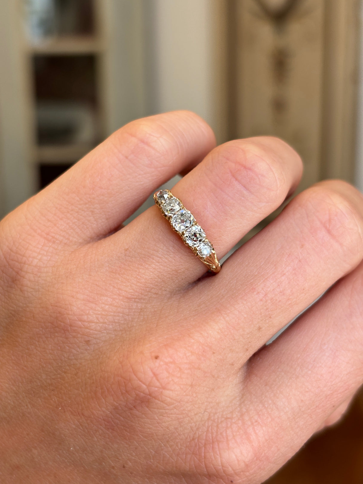Antique Victorian old-mine diamond five-stone ring featuring five graduated old-mine cut diamonds in a classic carved setting, worn on a hand.