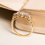 Antique Victorian five-stone ring featuring graduating old-mine cut diamonds with intricate hand-carved gold scrollwork shoulders.