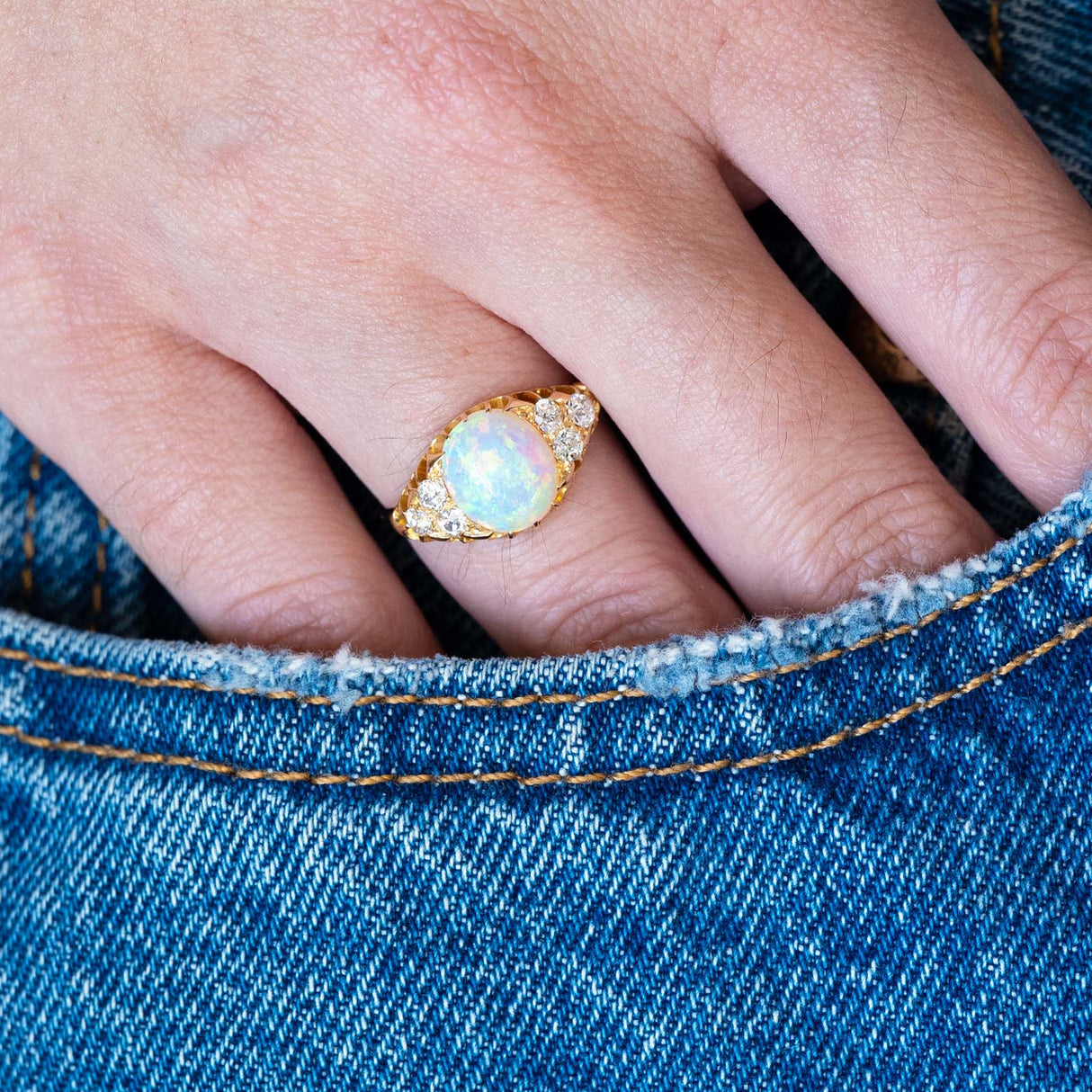 Antique Victorian opal and diamond ring worn on hand with blue denim pocket detail.