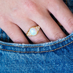Antique Victorian opal and diamond ring worn on hand with blue denim pocket detail.