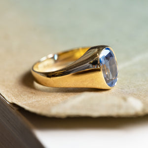 Antique Victorian sapphire single-stone ring displayed on antique book pages with polished gold setting.