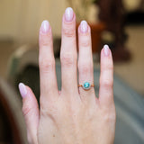 Antique cluster ring worn on hand with vivid blue zircon and diamond surround.