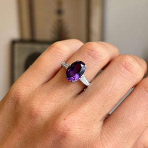 Close-up of an antique Art Deco platinum ring featuring a vivid purple amethyst flanked by diamonds, highlighting geometric lines, colour contrast and refined 1930s craftsmanship.