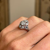 Antique Art Deco sapphire and diamond cluster ring in platinum worn on hand, featuring a vivid blue sapphire surrounded by sparkling old-cut diamonds, showcasing elegant 1920s craftsmanship against a softly lit interior backdrop.