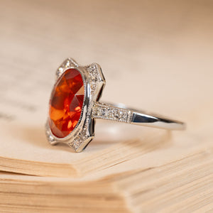 Antique Art Deco fire opal and diamond halo ring with a vibrant oval fire opal surrounded by old-cut diamonds and delicate detailing.
