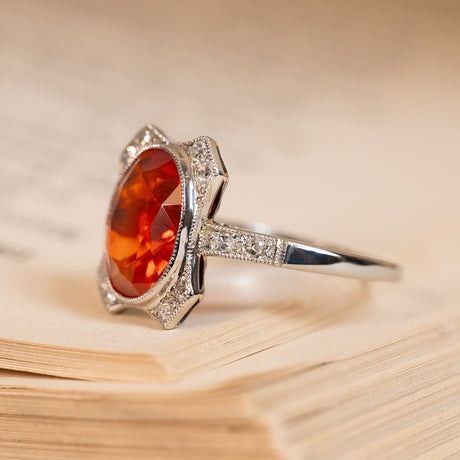 Antique Art Deco fire opal and diamond halo ring with a vibrant oval fire opal surrounded by old-cut diamonds and delicate detailing.