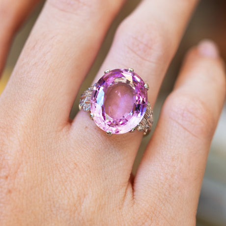 A close up of an Art Deco pink topaz and diamond cocktail ring with oval pink topaz and diamond shoulders on hand.