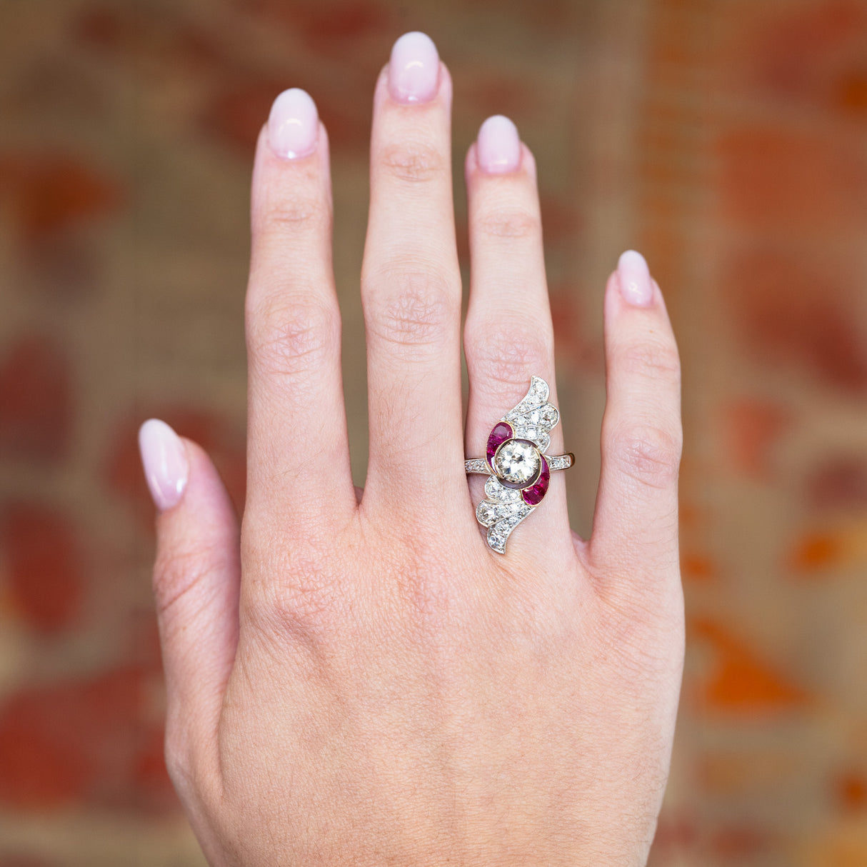 Art nouveau diamond and ruby cocktail ring worn on hand with sculptural design.