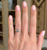 Blue sapphire and diamond engagement ring with an oval blue sapphire centre stone and diamond-set trefoil shoulders in the form of laurel leaves, displayed on a hand.