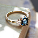 emerald cut blue sapphire ring with diamond cluster in yellow gold