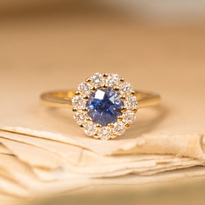 Bright blue sapphire and diamond cluster engagement ring featuring a vivid round sapphire surrounded by sparkling diamonds in yellow gold.