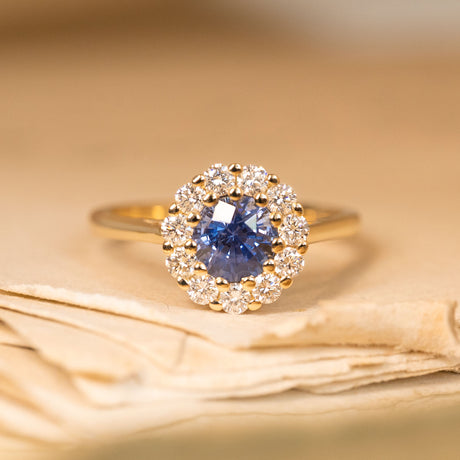 Bright blue sapphire and diamond cluster engagement ring featuring a vivid round sapphire surrounded by sparkling diamonds in yellow gold.